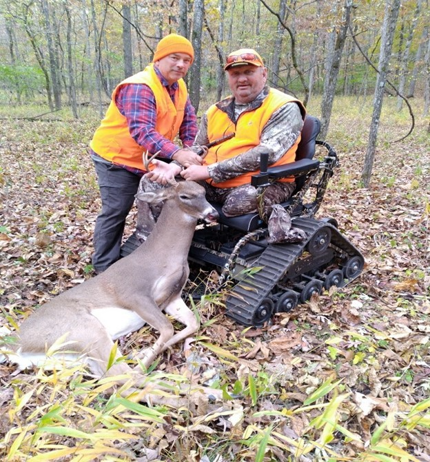 A hunter in a powered wheelchair holding his trophy buck after a successful hunt