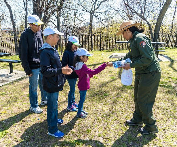 Outside in the park's picnic area, a female Paterson Great Falls Ranger gives badges out to four new Junior Rangers after completing their booklets and ball cap design activity.