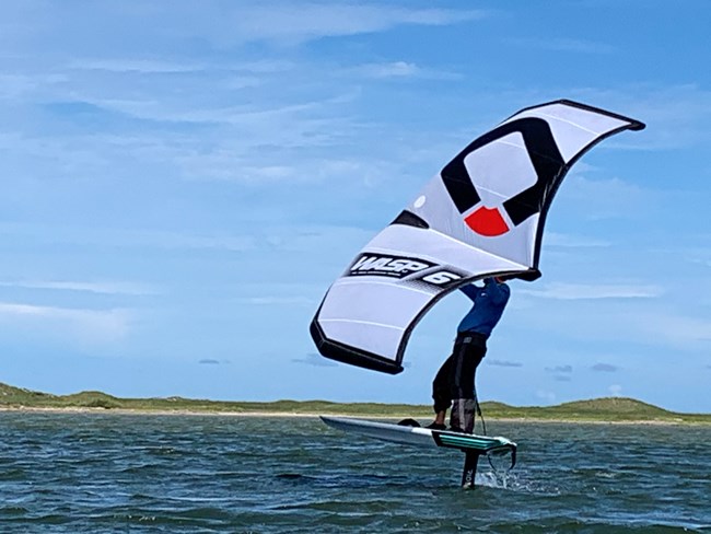 A person standing on a windsurfing board in the water while holding a sail