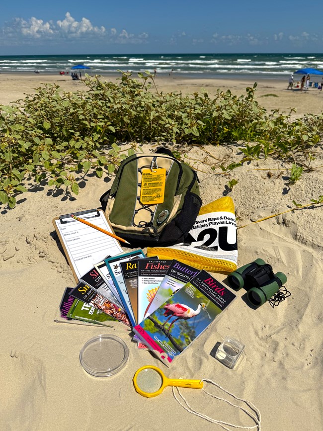 A backpack with educational supplies sitting in the sand.