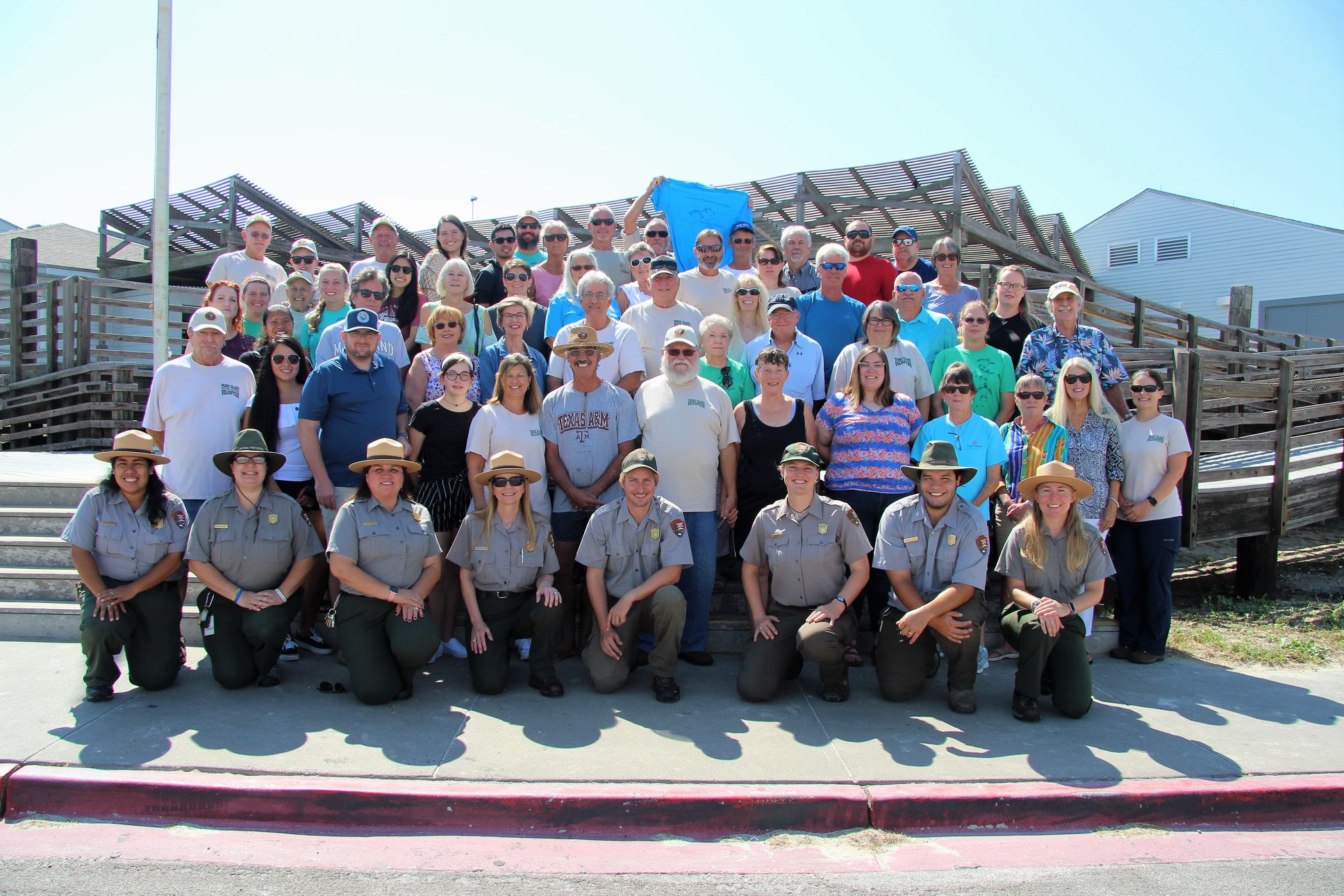 Over fifty smiling people gathered together with uniformed park service staff kneeling in front.