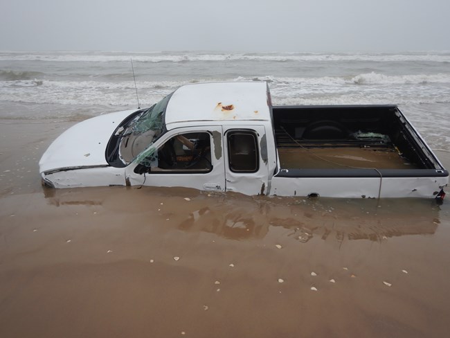 A white pickup truck stuck in the sand and flooded with water