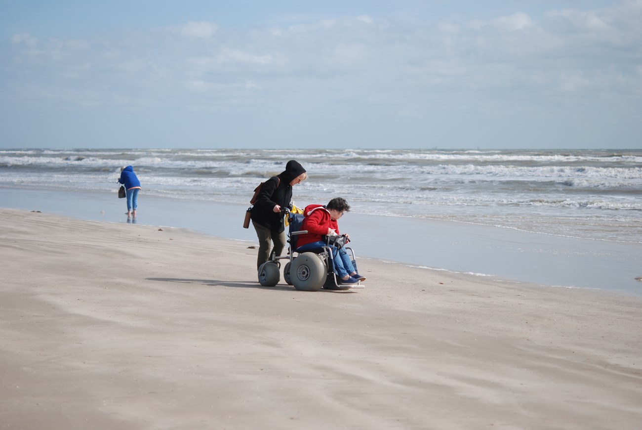 A person rides in a beach wheelchair on the beach
