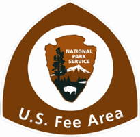 A brown sign with the NPS arrowhead logo with the words US Fee Area
