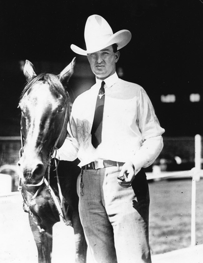 Man with cowboy hat standing next to a horse