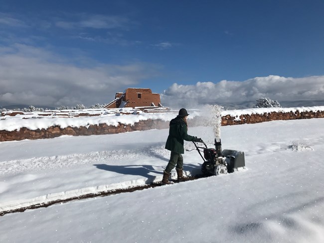 Park staff using snow blower in front of adobe mission church