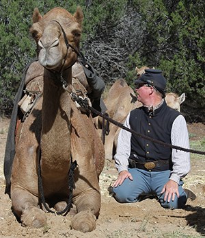 camel reenactor in period uniform sits next to a camel