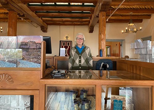 Pueblo Revival style interior of historic inn, woman behind counter with books and other items around.