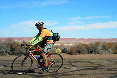 Colorful bicyclist against a blue sky and the red part of the Painted Desert.