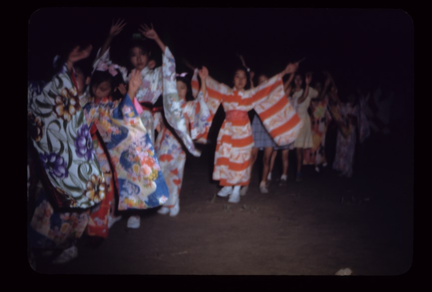 A line of young girls holding their hands up in the air while wearing colorful kimonos.