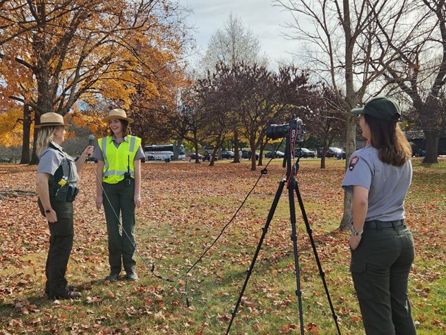 A park ranger faces two young individuals filming with a camera