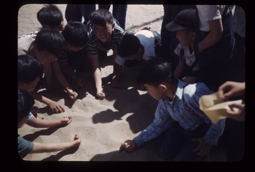 A group of kids playing with marbles on the ground.