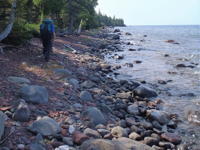 A lone backpacker treks along a rocky shoreline of Lake Superior.