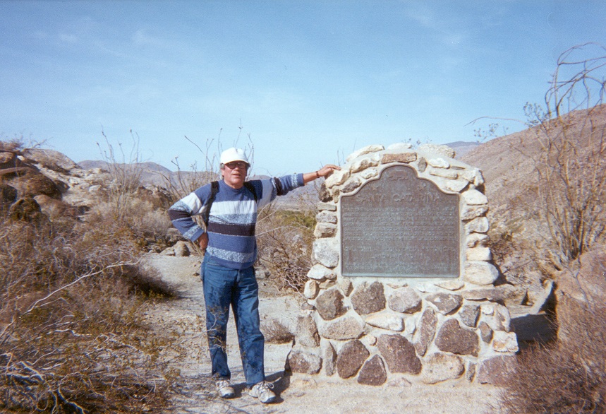 Man standing in a desert next to a large stone historical marker