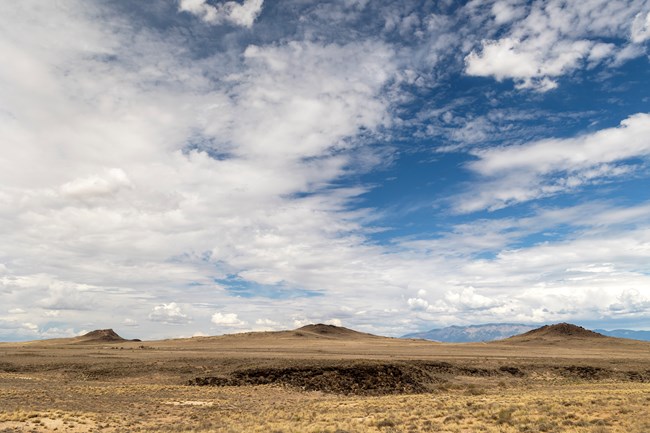 Three volcanoes under a partly cloudy sky with a mountain in the distance.