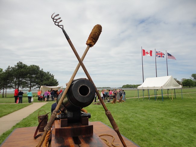 A cannon facing toward the camera with groups of people standing around historic tents in the background.