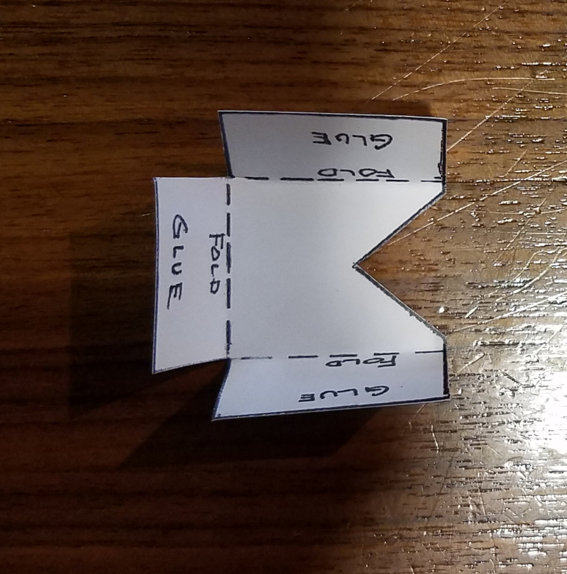 Small piece of paper with three folds along dotted lines. The piece of paper says fold and glue in three locations.