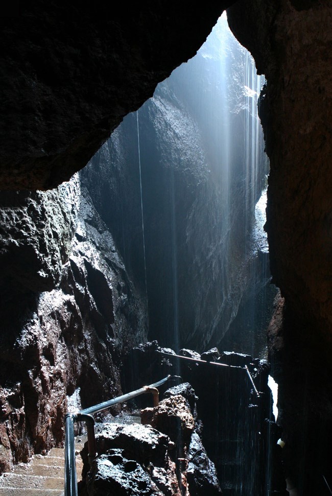 Stairs lead down into the depths of a cave as a misty waterfall streams down overhead.
