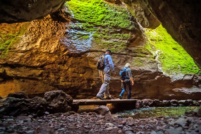 A male and female hiker walk into a cave.