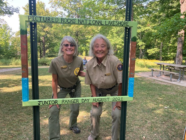 Two volunteers pose inside a painted wooden frame