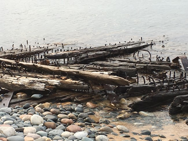 Wooden structure washed ashore along a beach. Iron nails are sticking out of the wood.
