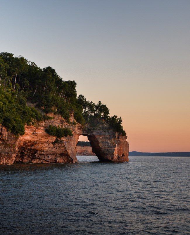 A sandstone arch rising out of Lake Superior at sunset