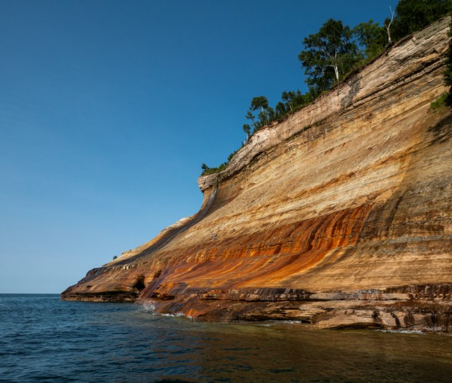 Mineral stained cliffs rise out of Lake Superior with a thin waterfall cadcading over them.