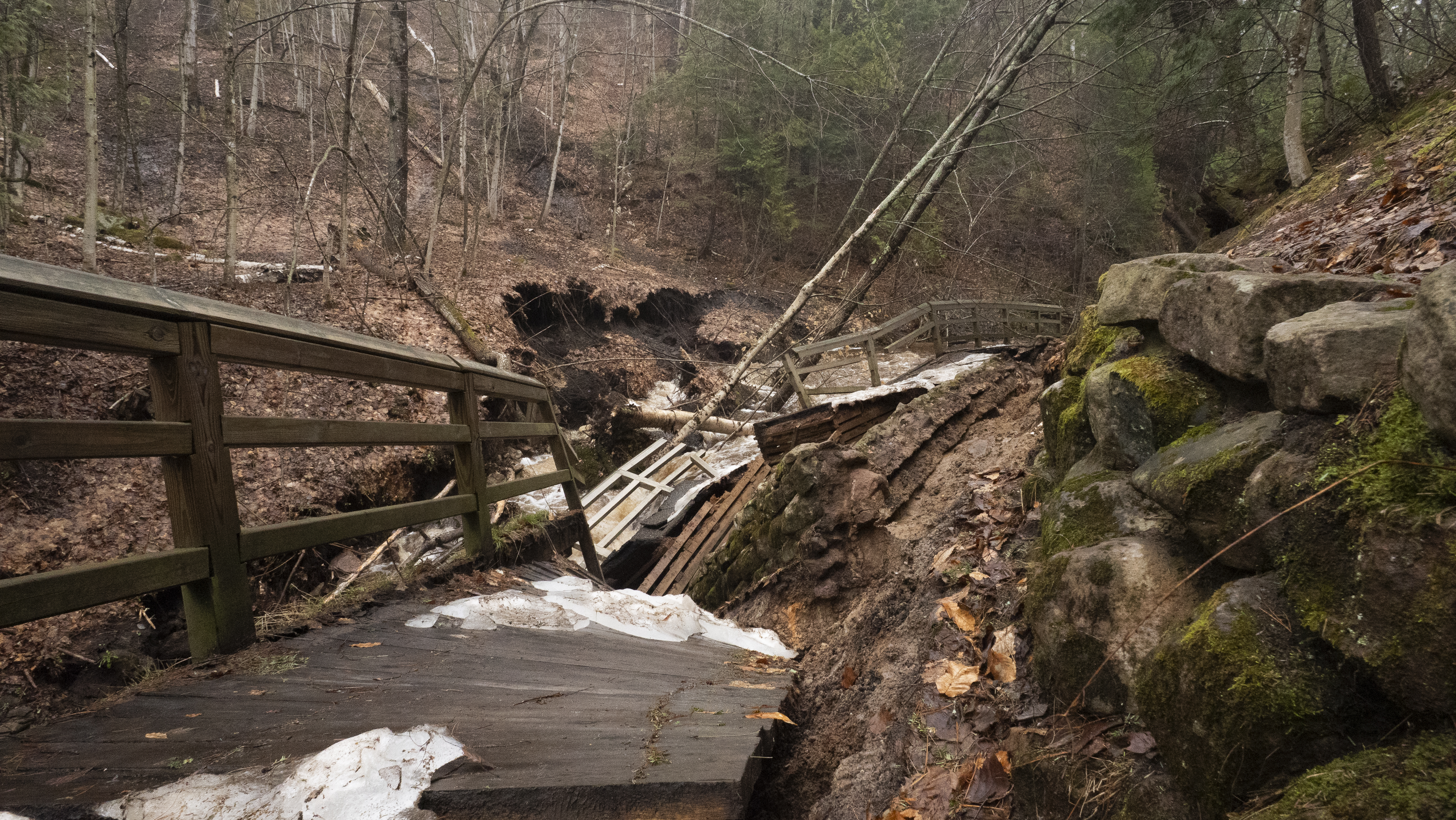 A badly damaged, paved trail falling into the river next to it.