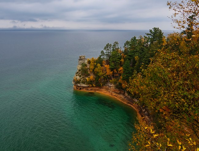 A sandstone formation rises out of Lake Superior surrounded by autumn leaves.