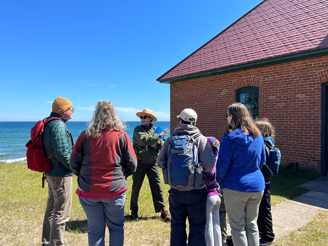 A ranger gives a tour at in front of a brick building