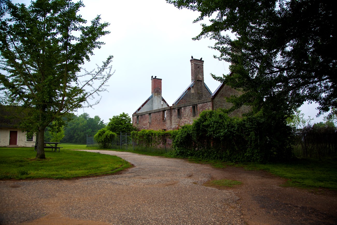 The brick ruins of a two story house surrounded by an overgrown fence