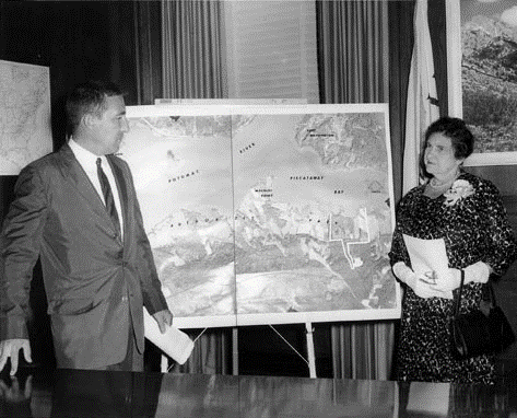 A black and white photo of a man and woman on either side of a large poster