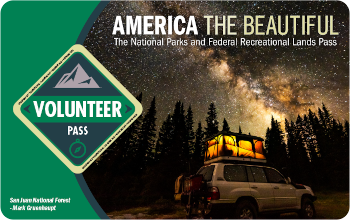 Image of the 2022 Interagency Volunteer Pass with a 4-wheel drive vehicle with a tent on top under a starry night sky.