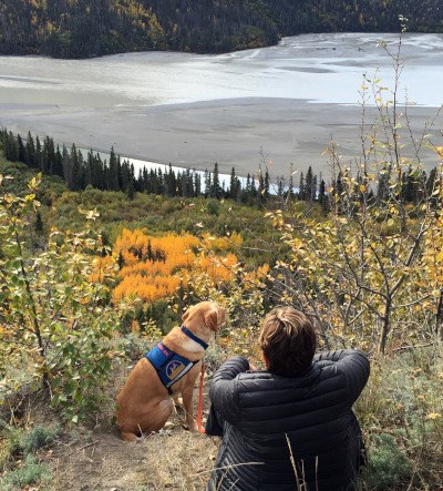 Woman and her service dog take in the view of Alaskan river and woods