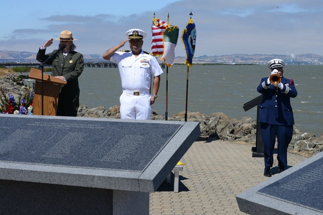 Two uniformed people stand at attention while a third plays a bugle.
