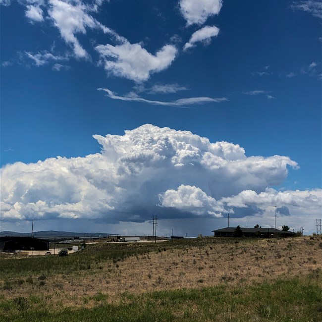 A large storm cells looms in the distance over an open prairie.