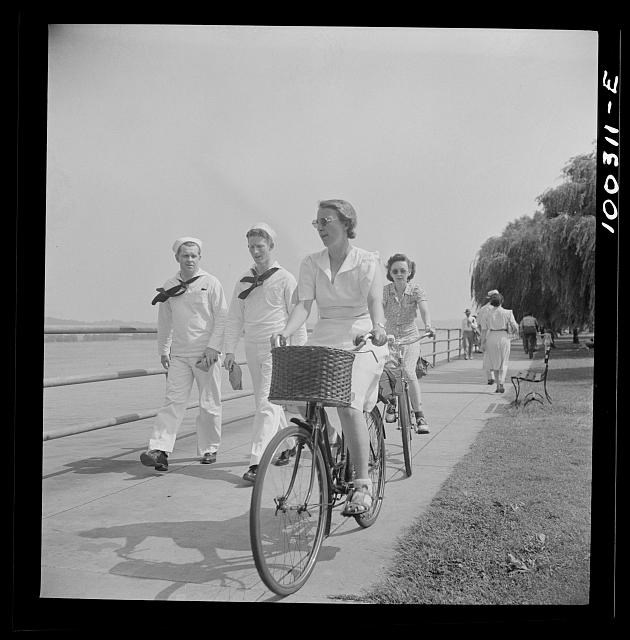 black and white photo of two women riding bikes along a river