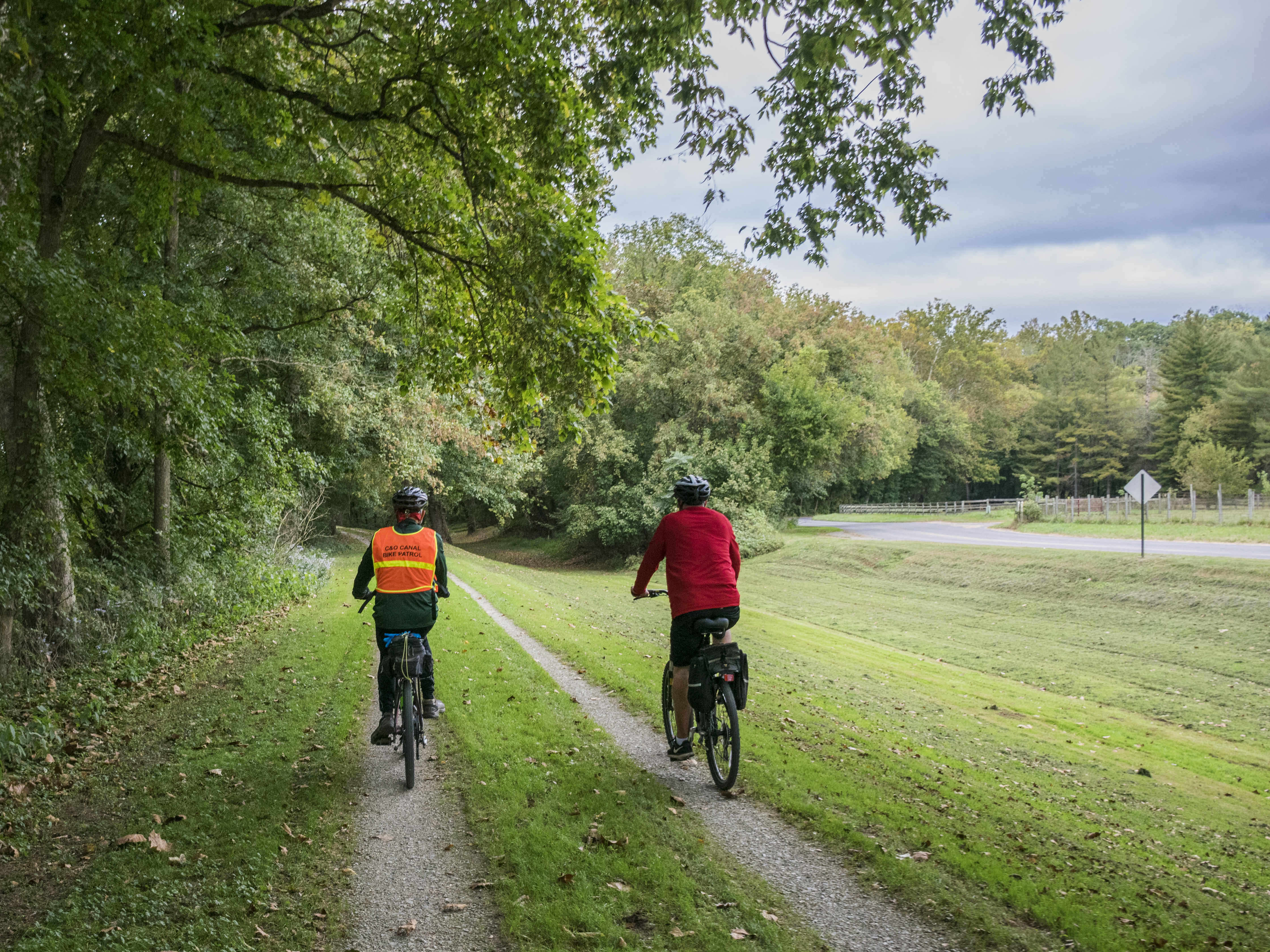 Two bikers travel along the grass and gravel towpath
