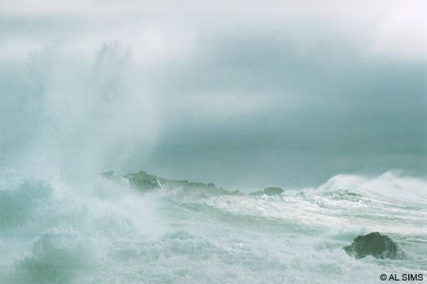 Large white-capped ocean waves crashing on rocks during a storm.
