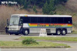 A white coach-sized bus painted with a rainbow-colored horizontal stripe below the windows on its sides.