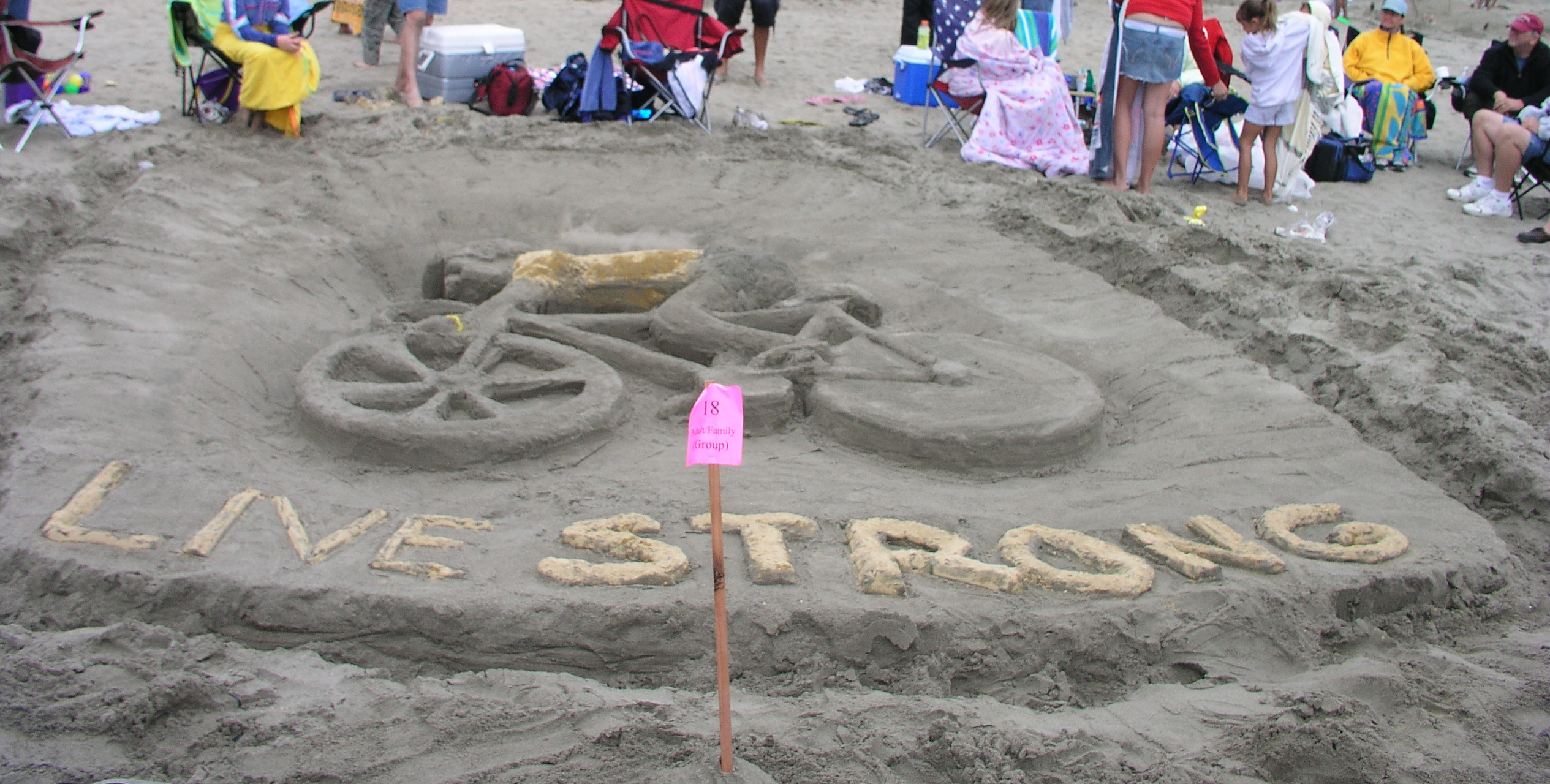 A bas-relief sand sculpture of a person wearing a yellow jersey and yellow wrist band riding a bicycle with the words "Live Strong" under the bicycle.