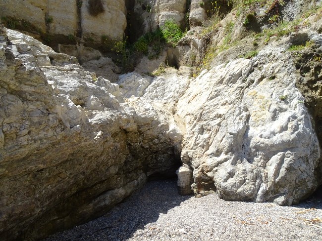 A light-colored wall of rock rising above a coarse sand beach.