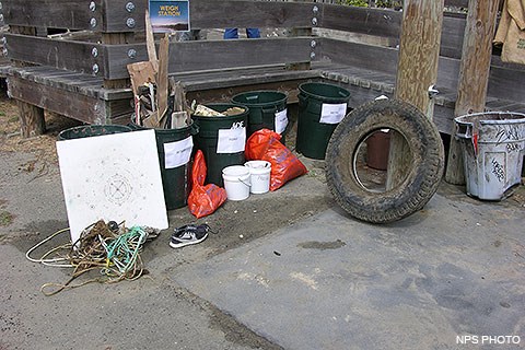 Garbage that was collected from Drakes Beach included (from left to right, some of which are in dark green garbage cans): ropes, a large white cutting board, wood, a pair of sneakers, foam, a three-foot diameter tire, and a light blue garbage can.