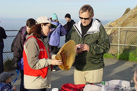A female volunteer in a red vest showing gray whale baleen to a male visitor.