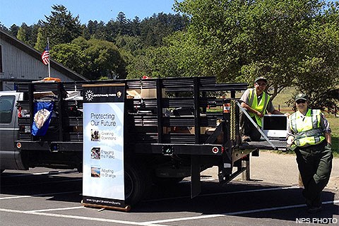 Two uniformed park employees loading electronic waste into a gray stake bed truck.