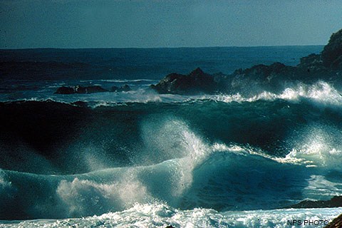 Large waves crashing on a beach and rocks.