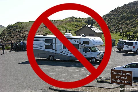 A large recreational vehicle parked in a small parking lot. A red circle with a diagonal line indicates that doing so is prohibited.