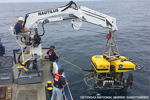 Three men on a ship hoisting a yellow remotely operated vehicle from the ocean.
