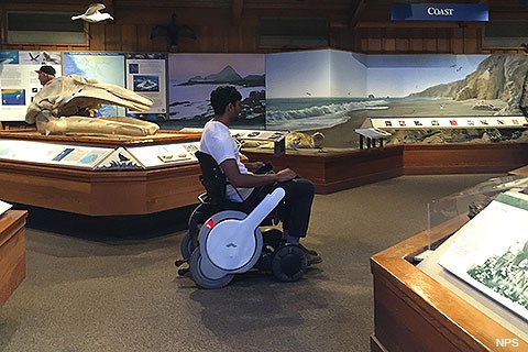 A person in a white motorized wheelchair among museum exhibits.