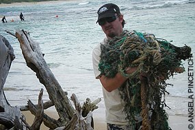A man carries an arm-full of marine debris on a beach.